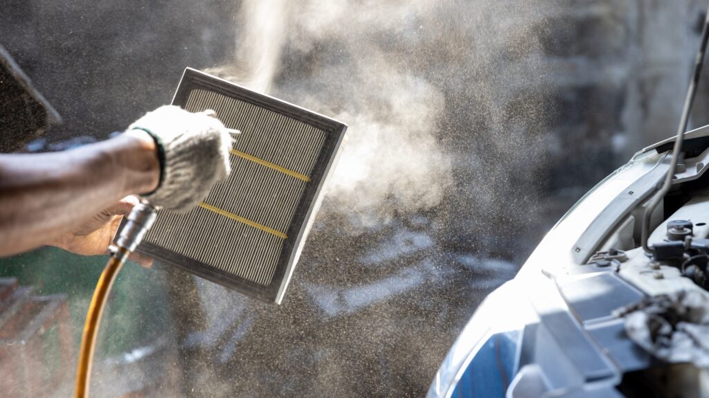 Mechanic cleaning dirty car air filter with air blow gun.